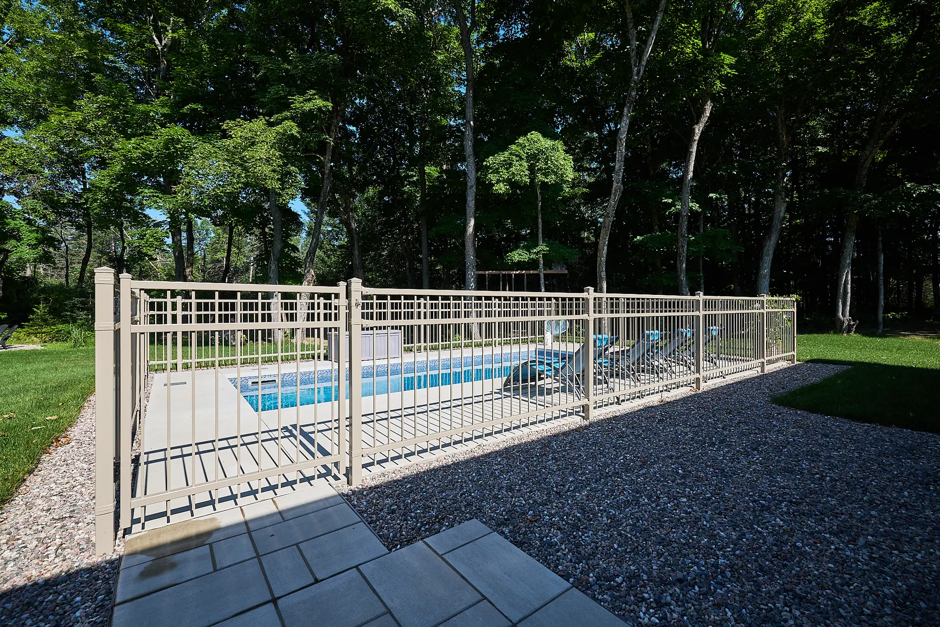 Inter Clôtures Sentinelle A fenced-in rectangular swimming pool with lounge chairs sits in a backyard surrounded by trees and green grass. Fence Installation Quebec