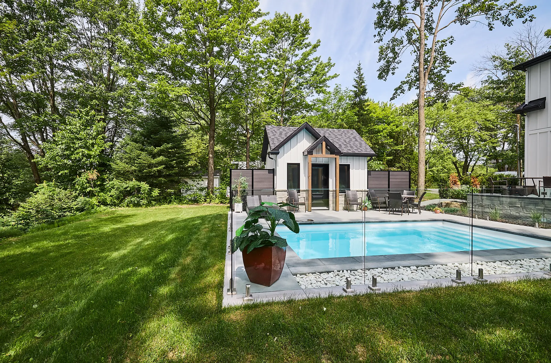 Inter Clôtures Sentinelle A small modern guesthouse and swimming pool with glass fencing are set in a green backyard surrounded by trees and lawn. Fence Installation Quebec