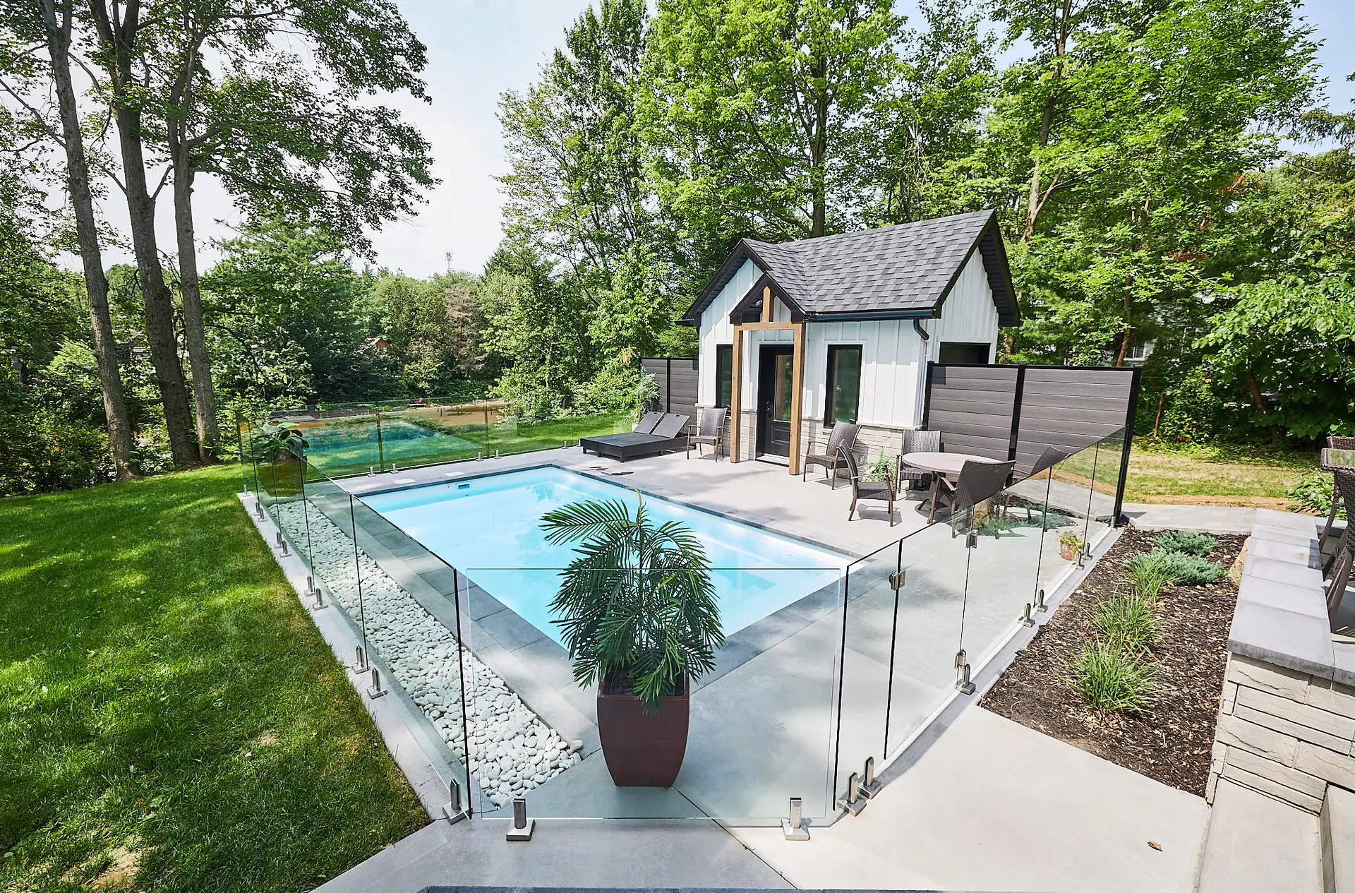 Inter Clôtures Sentinelle A small fenced-in pool with lounge chairs and a potted plant, next to a modern shed surrounded by trees and greenery. Fence Installation Quebec