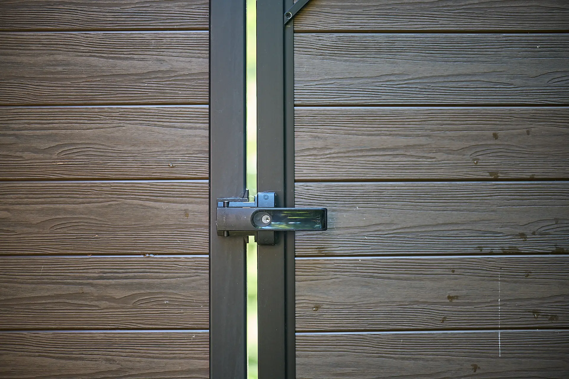 Inter Clôtures Sentinelle A padlocked metal latch secures a closed gate made of horizontal brown wooden planks, with a narrow gap allowing light through the center. Fence Installation Quebec