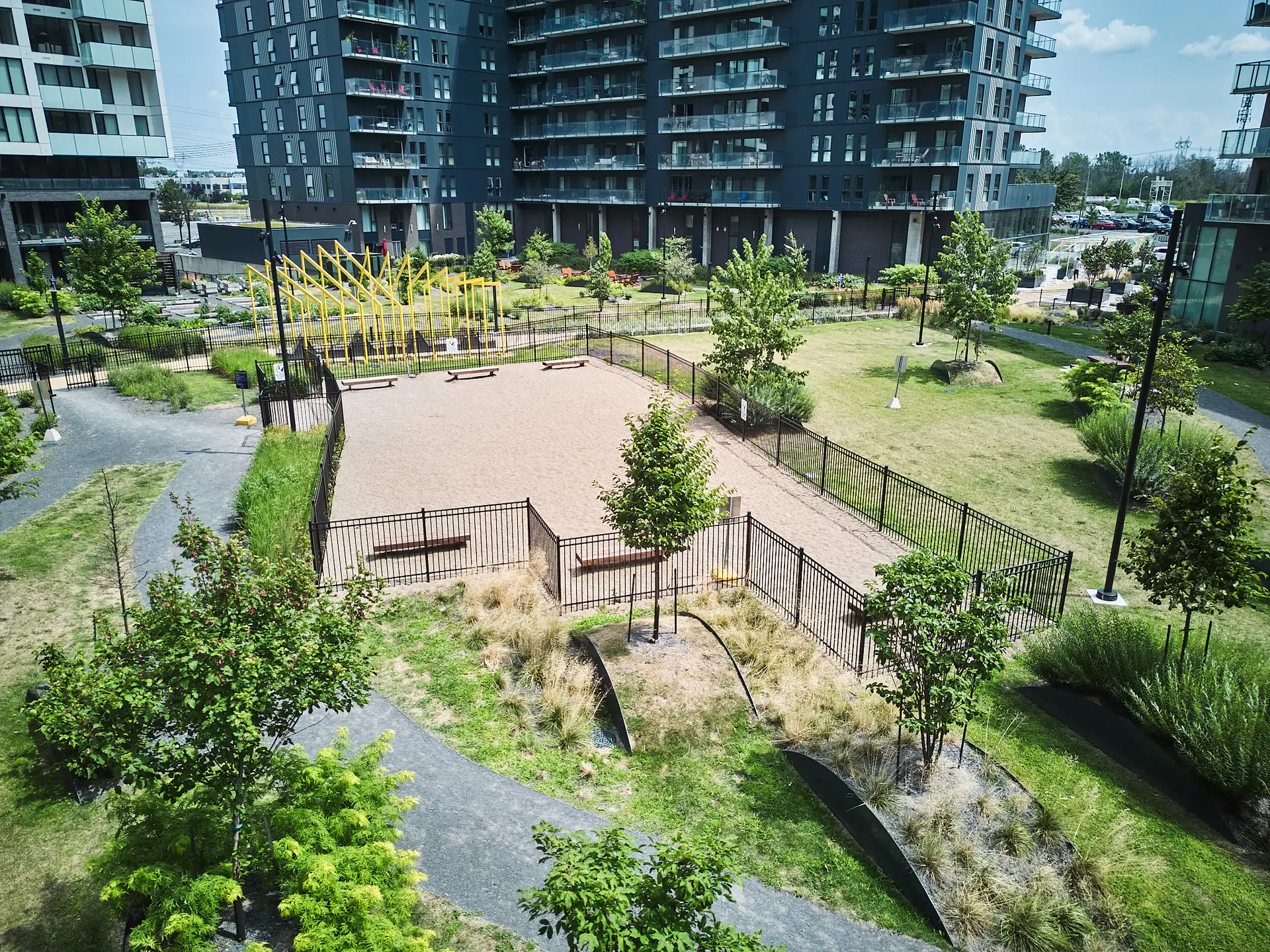 Inter Clôtures Sentinelle A fenced dog park with benches and gravel, surrounded by pathways, trees, and apartment buildings in an urban green space. Fence Installation Quebec